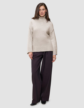 En kvinne har på seg en Women’s Chunky Soft Wool Knit Turtleneck Sugar Melange-genser og mørke bukser med vide ben.