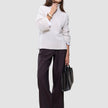 En kvinne kledd i en Women’s Chunky Soft Wool Knit Turtleneck Sugar Melange og mørke bukser med vide ben, som holder en svart håndveske.