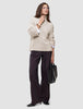 En kvinne har på seg en Women’s Chunky Soft Wool Knit Turtleneck Sugar Melange over en hvit skjorte og mørke bukser med vide ben.