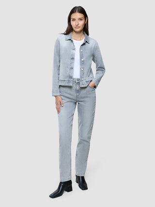 En kvinne viser frem en klassisk damedenimjakke i lys gråvasket utførelse, en hvit T-skjorte, matchende jeans og svarte ankelstøvler.
