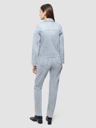 En kvinne sett bakfra, kledd i en «Women’s Classic Denim Jacket Light Grey Washed» og matchende jeans med svarte støvler.