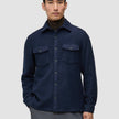En mann har på seg en dobbeltsidig ullskjorte i mørk marineblå i standardpassform over en brun turtleneck, noe som gjenspeiler et minimalistisk design.