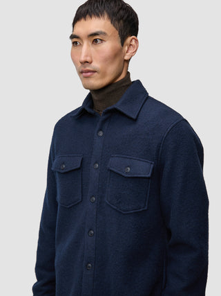 En mann har på seg en dobbeltsidig ullskjorte i mørk marineblå i standardpassform over en mørkebrun turtleneck.