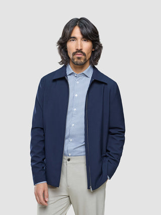 En mann iført en Ease Jacket Blue Nights over en blå- og hvitstripet skjorte med knapper og lyse bukser.