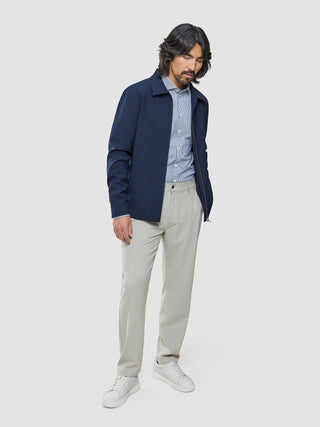 En mann i en Ease Jacket Blue Nights over en stripete skjorte med knapper, lyse bukser og hvite joggesko med 360°-stretch.