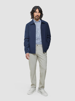 En mann kledd i en Ease Jacket Blue Nights, en stripete skjorte med knapper, lyse bukser og hvite joggesko.