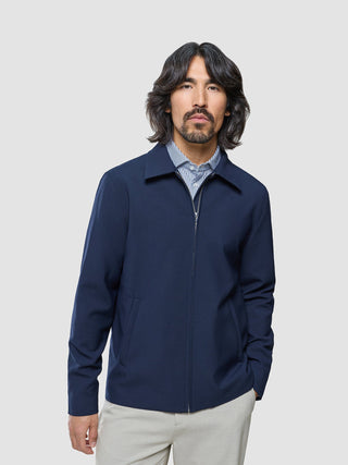 En mann med langt, mørkt hår, kledd i en marineblå Ease Jacket Blue Nights over en stripete skjorte med krage.