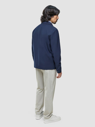 En mann sett bakfra, kledd i en Ease Jacket Blue Nights, lyse bukser og hvite joggesko.