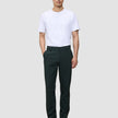 En mann har på seg en hvit T-skjorte, Ease Pants Regular Northern Pine og mørke skinnsko i en minimalistisk skandinavisk stil.