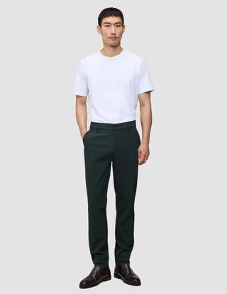En mann har på seg en hvit T-skjorte, Ease Pants Regular Northern Pine og mørke skinnsko i en minimalistisk skandinavisk stil.