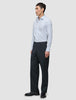 En mann i en Elevated Shirt Regular Classic Blue Striped – en lysblå skjorte med knapper – som er stappet ned i grå bukser og dressko.