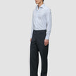 En mann i en Elevated Shirt Regular Classic Blue Striped – en lysblå skjorte med knapper – som er stappet ned i grå bukser og dressko.