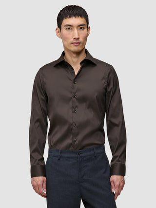 En mann har på seg en mørkebrun Elevated Shirt Slim, som er stappet inn i mørke bukser.