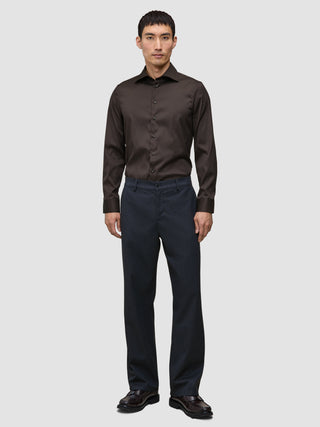 En mann kledd i en mørkebrun Elevated Shirt Slim, mørke bukser og mørke skinnsko.