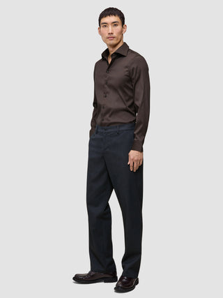 En mann kledd i en mørkebrun Elevated Shirt Slim-skjorte i pima-bomull og antrasittgrå bukser.