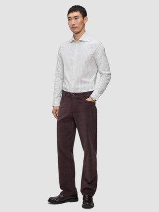 En mann i en Elevated Shirt Slim med lysegrå striper, mørkebrune bukser og mørke loafers.