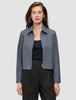 En kvinne har på seg en Essential Short Zip Jacket Dark Grey Melange – en minimalistisk jakke med krage og glidelås – over en svart topp.