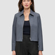 En kvinne har på seg en Essential Short Zip Jacket Dark Grey Melange – en minimalistisk jakke med krage og glidelås – over en svart topp.