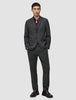 En mann i en Motion Blazer Regular Pepper Grey-jakke, matchende bukser og en mørk skjorte med knapper, samt loafers.