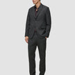 En mann kledd i en Motion Blazer Regular i fargen Pepper Grey og matchende bukser, sammen med en mørk skjorte med knapper.