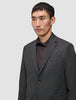 En mann har på seg en Motion Blazer Regular i fargen Pepper Grey over en mørk skjorte med knapper.