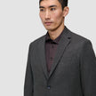 En mann har på seg en Motion Blazer Regular i fargen Pepper Grey over en mørk skjorte med knapper.