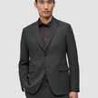 En mann som har på seg en grå Motion Blazer Slim Pepper Grey over en mørk skjorte med knapper.