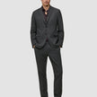 En mann kledd i en Motion Blazer Slim Pepper Grey-jakke, matchende bukser, mørk skjorte og loafers.