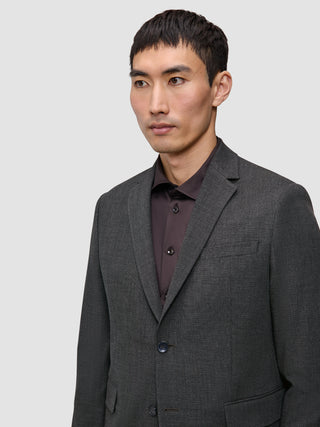 En mann som har på seg en skreddersydd Motion Blazer Slim Pepper Grey-blazer over en mørk skjorte med knapper.