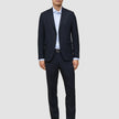 En mann kledd i Motion Suit-bukser i størrelse Regular i fargen Midnight Blue, med en lyseblå skjorte og mørke skinnloafers.