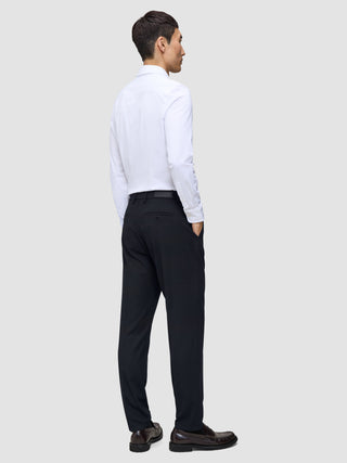 En mann i hvit skjorte og en Midnight Blue Motion Suit Pants Regular-bukse står med ryggen til kameraet.