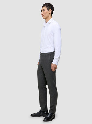 En mann i en hvit skjorte med knapper og grå Motion Suit-bukser i Regular Pepper Grey står sett i profil.