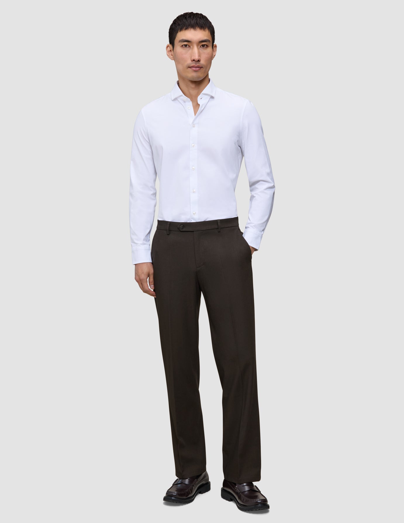 En mann i en hvit skjorte med knapper og Motion Suit-bukser i modellen Relaxed Cognac, med et rent skandinavisk design.
