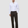 En mann i en hvit skjorte med knapper og Motion Suit-bukser i modellen Relaxed Cognac, med et rent skandinavisk design.