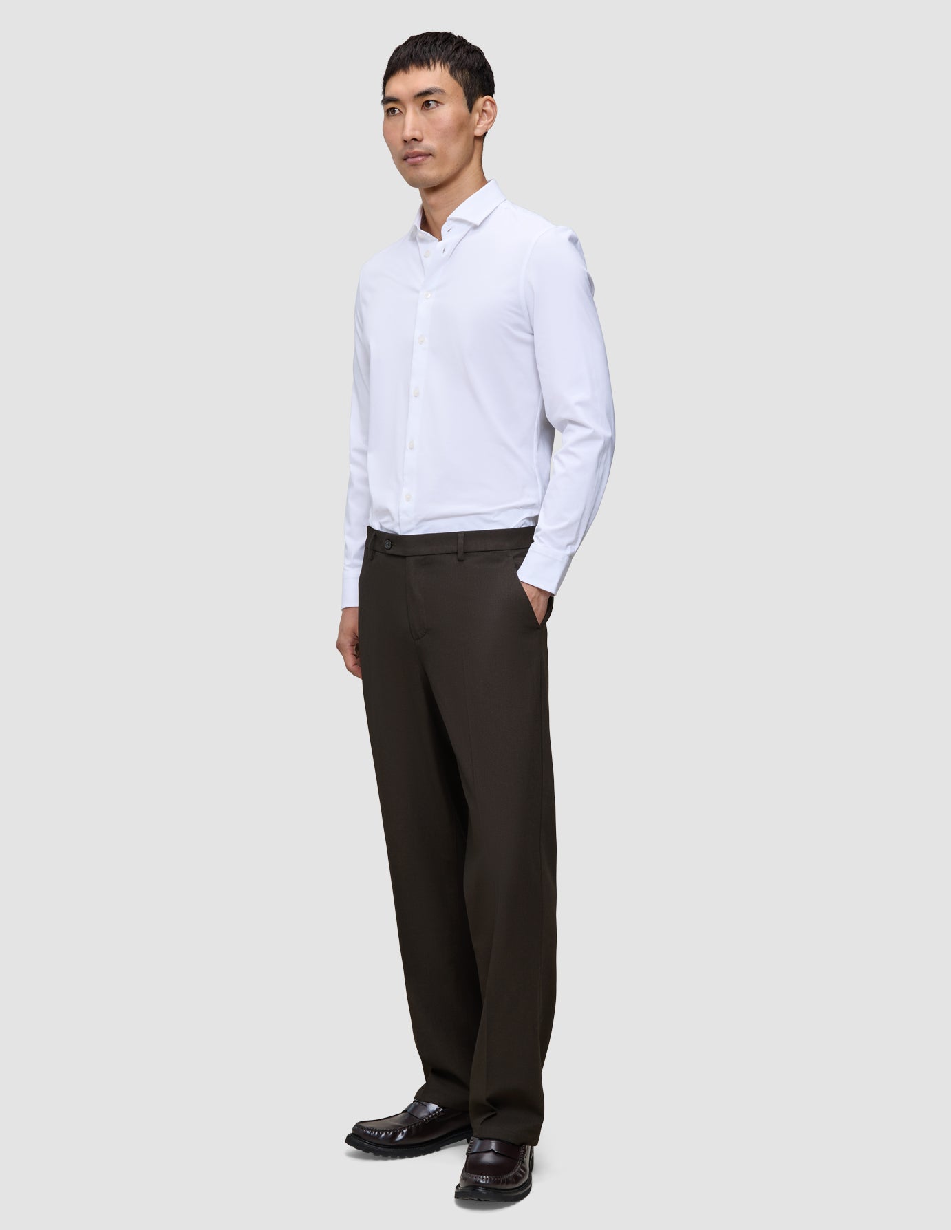 En mann i en hvit skjorte og Relaxed Cognac Motion-dressbukser med avslappet passform.