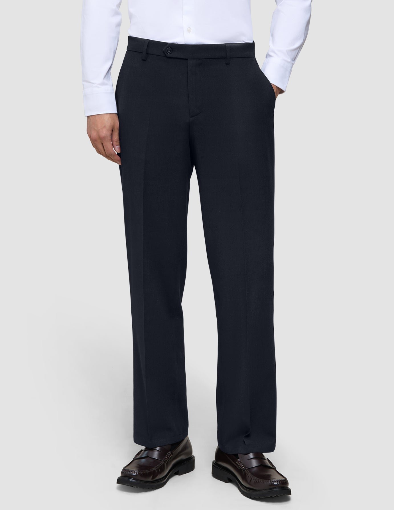 En person som har på seg Motion Suit-bukser i modell Relaxed i fargen Midnight Blue, en hvit skjorte med knapper og mørke loafers.