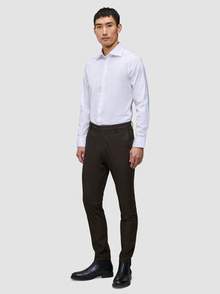 En mann har på seg en hvit skjorte, Motion Suit Pants Slim Cognac og svarte støvler i et rent, skandinavisk design.