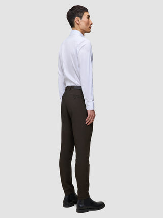 En mann sett i profil har på seg en hvit skjorte, Motion Suit-bukser i Slim-modell i fargen Cognac og svarte lærstøvler.