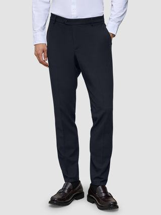 Motion Suit Pants Slim – Midnattsblå dressbukser i slim fit, kombinert med en hvit skjorte med knapper og brune loafers.