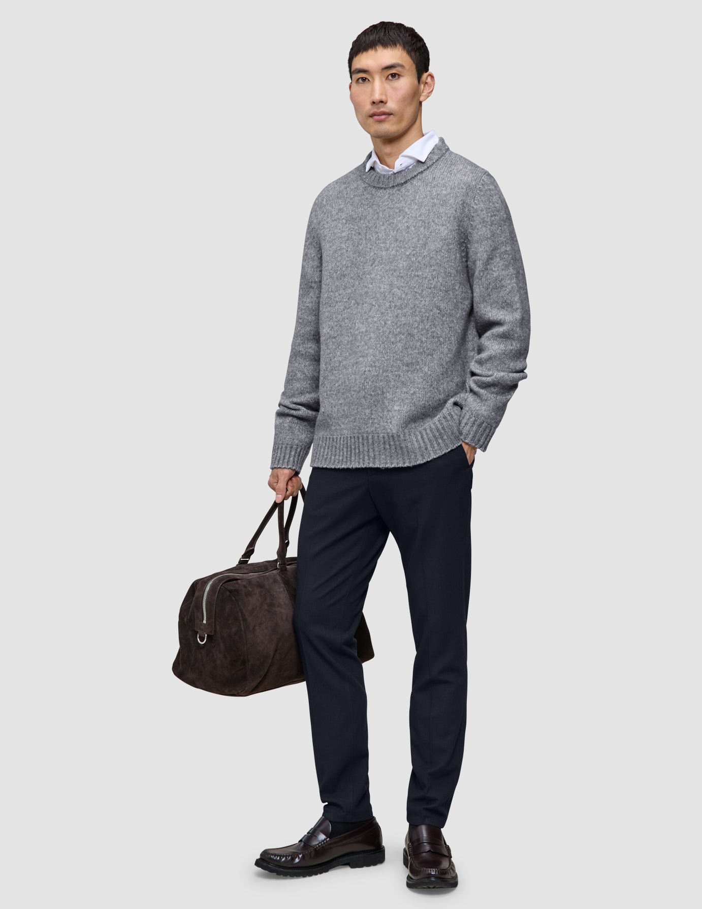 En mann i en grå genser og Motion Suit-bukser i slim-passform i midnattsblått, som holder en brun skinnreiseveske.