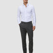 En mann kledd i en hvit skjorte med knapper, Motion Suit Pants Slim Pepper Grey og svarte loafers.