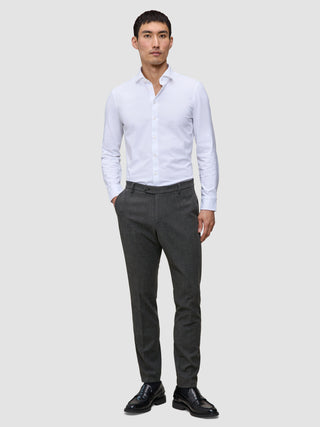 En mann kledd i en hvit skjorte med knapper, Motion Suit Pants Slim Pepper Grey og svarte loafers.