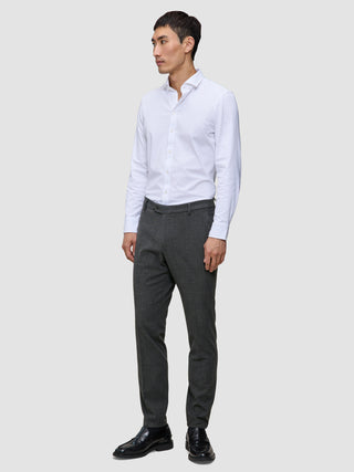 En mann i en hvit skjorte med knapper, Motion Suit-bukser i Slim-modell i fargen Pepper Grey og svarte dressko.