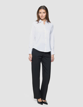 En kvinne kledd i en hvit «Women Oxford Shirt White Regular» og svarte bukser, som gjenspeiler et rent skandinavisk design.
