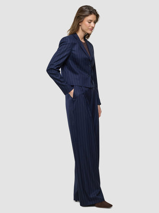 En kvinne står i profil, kledd i en «Women Raina Short Blazer Night Sky Pinstripe» og matchende bukser med vide ben.