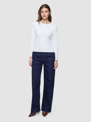 En kvinne som har på seg en hvit «Women Rib»-T-skjorte med lange ermer og mørkeblå jeans med vide ben.