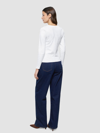 En kvinne sett bakfra, kledd i en hvit «Women Rib»-T-skjorte med lange ermer og mørkeblå jeans.