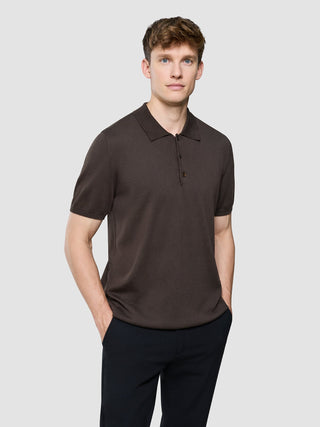 En mann kledd i en mørkebrun Seamless Core Knit-poloskjorte med korte ermer, med hendene i lommene.