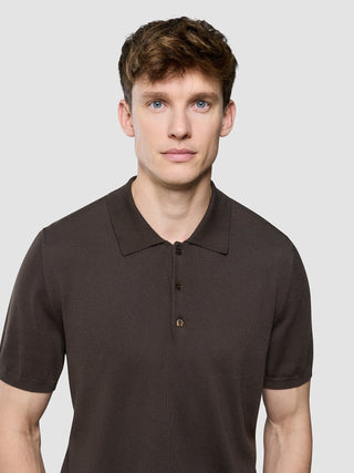 En mann som har på seg en mørkebrun Seamless Core Knit-poloskjorte med korte ermer.