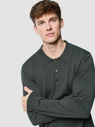 En mann med armene i kors, kledd i en Seamless Core Knit langermet polo i fargen «Green Night».